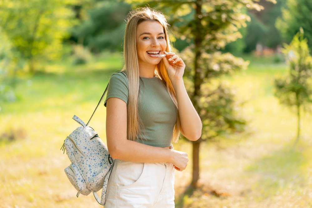 Smiling Young Woman Outdoors After Invisalign Treatment – Invisalign in Irvine Happy woman with a bright smile standing outdoors, showing off straight teeth after Invisalign treatment – Invisalign in Irvine