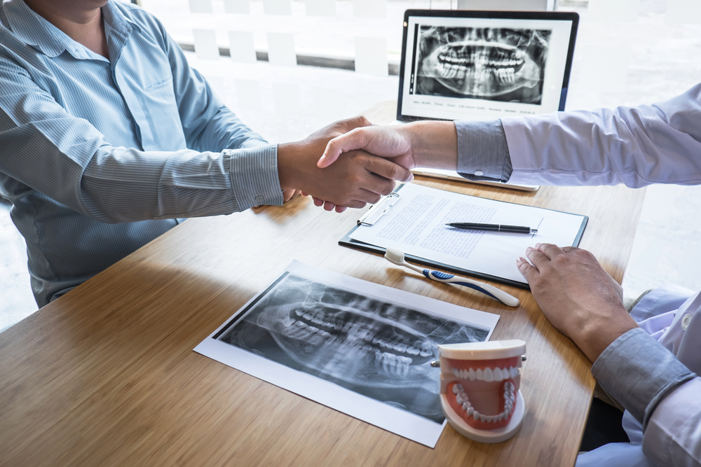 Patient shaking hands with a dentist during a consultation while reviewing dental X-rays and treatment plans – Anderson Family Dental