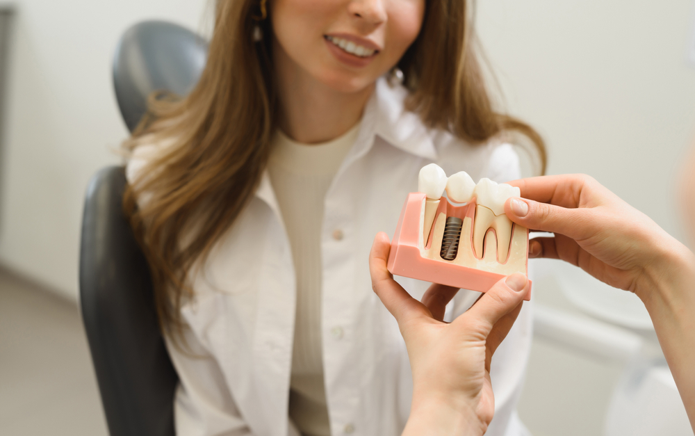 Dentist Explaining Dental Implant Model – Dental Implants Lake Forest CA Dentist showing a dental implant model to a smiling patient during consultation – Dental Implants Lake Forest CA