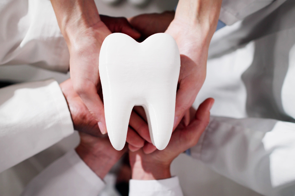 Dentists holding a large tooth model together, symbolizing teamwork and quality care – Anderson Family Dental