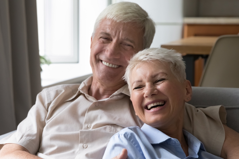 Happy Senior Couple Smiling at Home After Restorative Treatment – Dental Implants Irvine Older couple relaxing and smiling confidently after receiving dental implants – Dental Implants Irvine