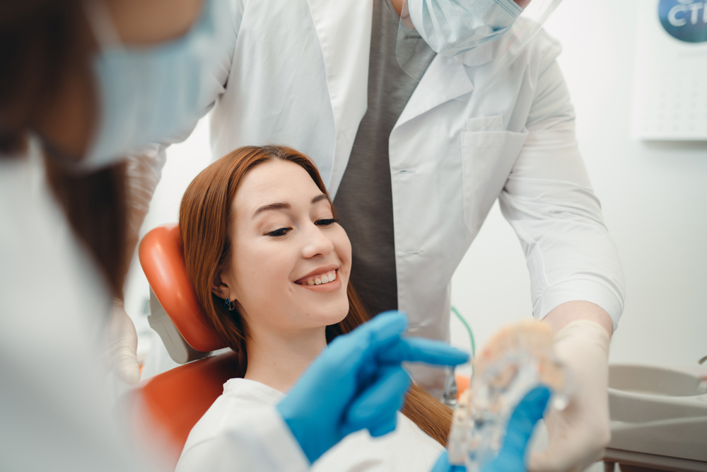 Smiling patient sitting in a dental chair while a dentist explains treatment using a dental model – Anderson Family Dental