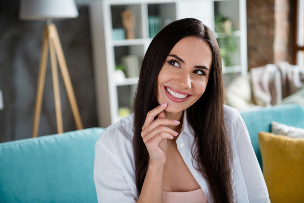 Confident Woman with a Bright Smile – Teeth Whitening in Irvine Smiling woman sitting on a sofa with radiant white teeth after professional whitening treatment – Teeth Whitening in Irvine