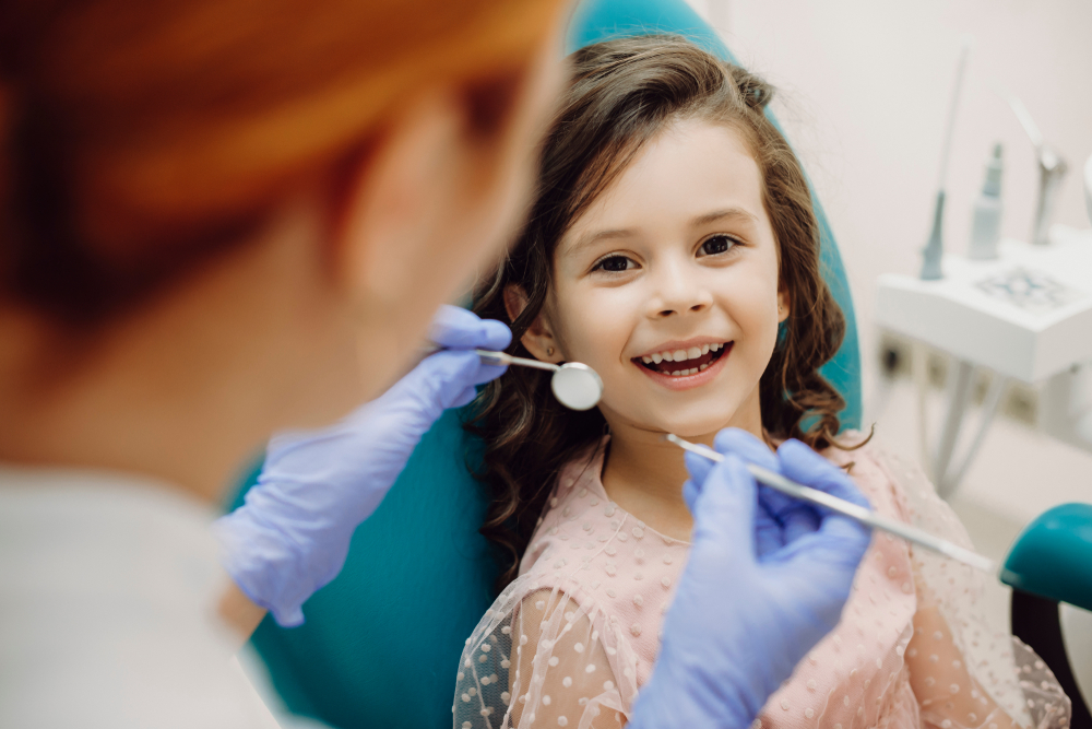 Smiling young girl sitting in a dental chair during a routine checkup with a dentist – Anderson Family Dental
